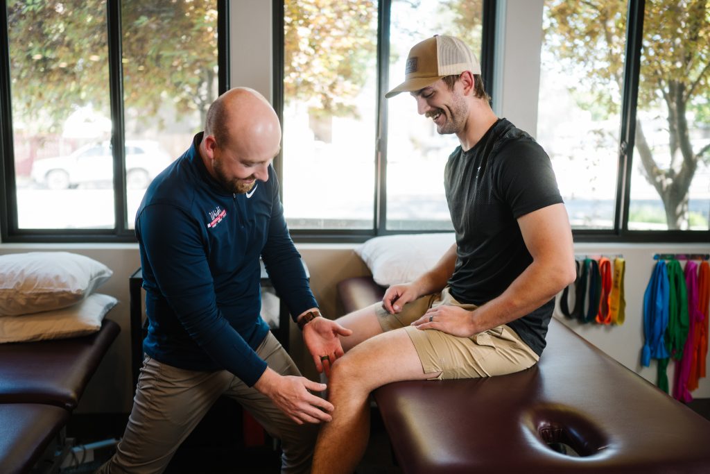 Physical therapist testing a patient's knee pain as she bends and straightens her leg on a treatment table